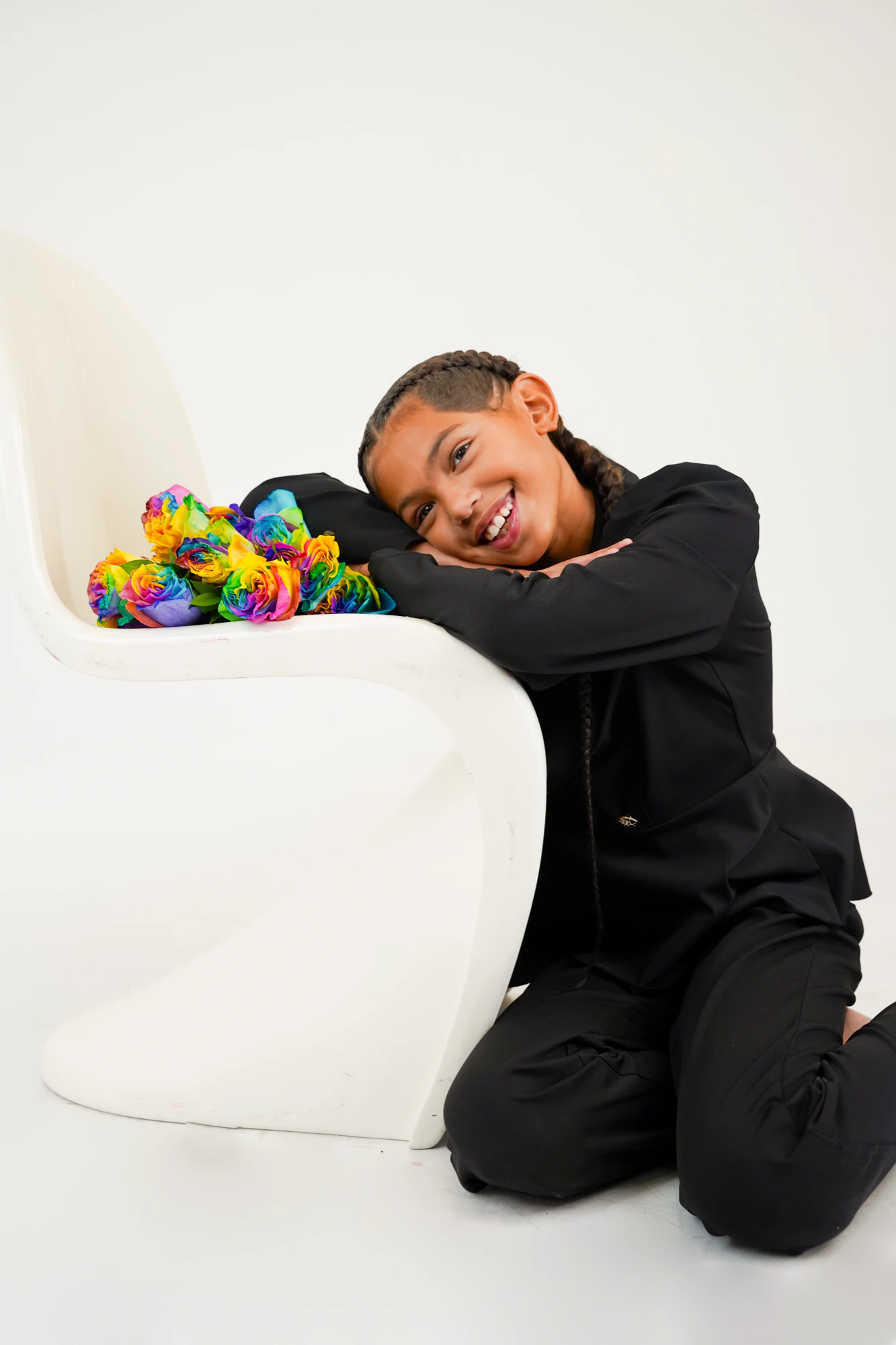 Amaya resting her head on her arms on a white chair, next to a bunch of rainbow roses